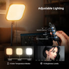 A hand operates the NEEWER L220 Bi Color Panel Light, adjusting its brightness and color temperature settings during a video call.